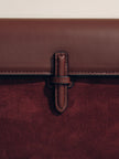 Close-up of a brown leather strap on a maroon bag with a beige background