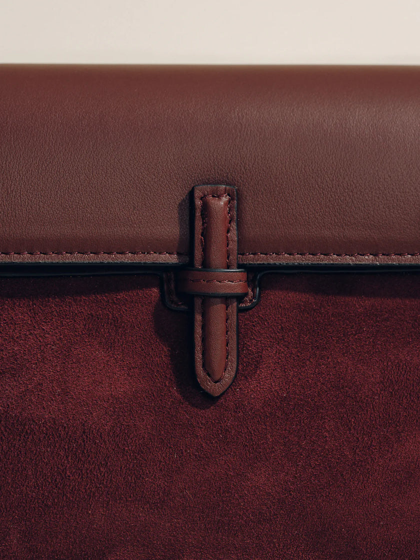 Close-up of a brown leather strap on a maroon bag with a beige background