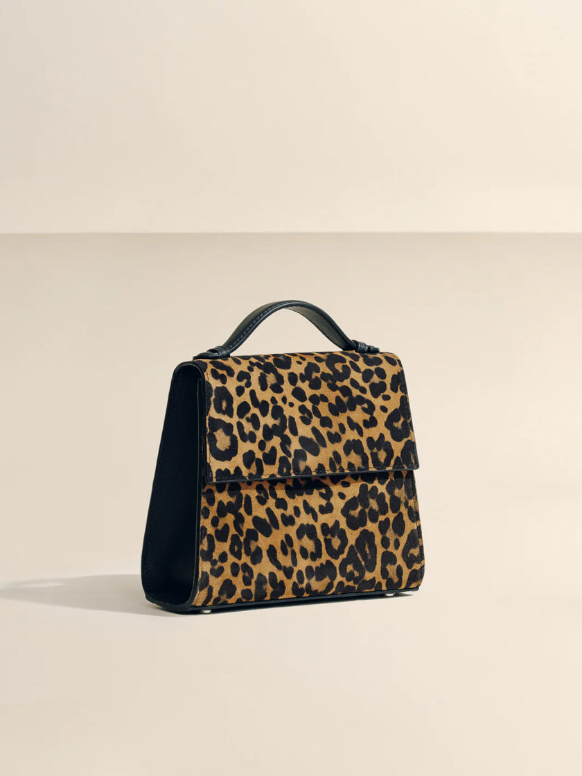 Leopard print handbag with black accents on a beige background