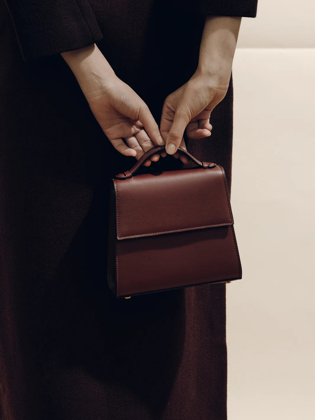 Person holding a brown leather handbag against a neutral background