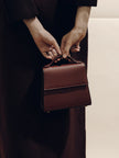 Person holding a brown leather handbag against a neutral background