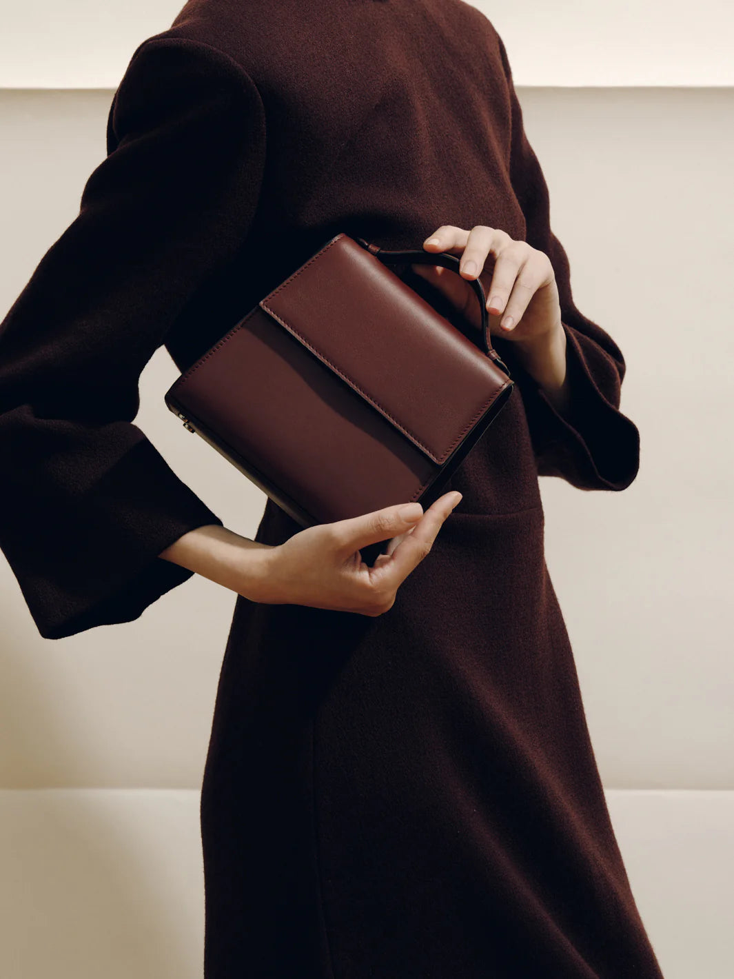 Person holding a brown leather clutch against a neutral background