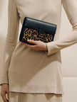 Person holding a black clutch with leopard print pattern against a neutral background