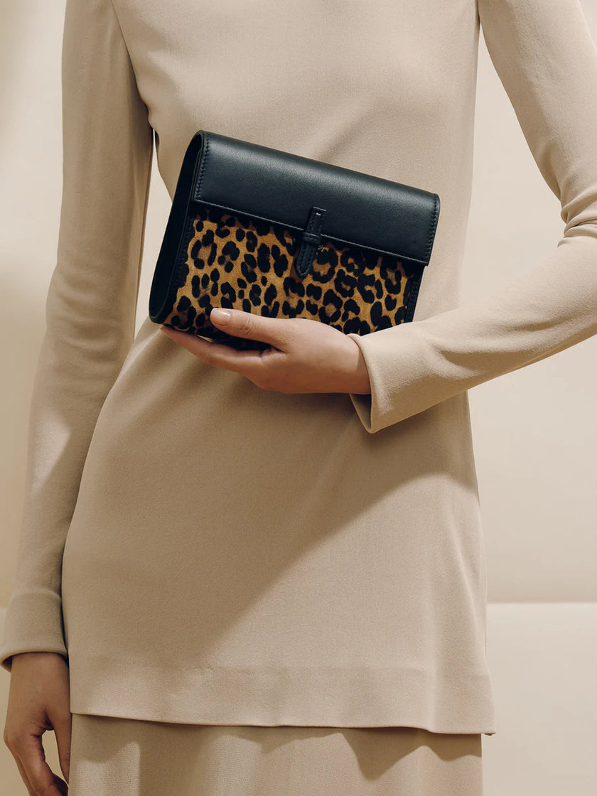 Person holding a black clutch with leopard print pattern against a neutral background