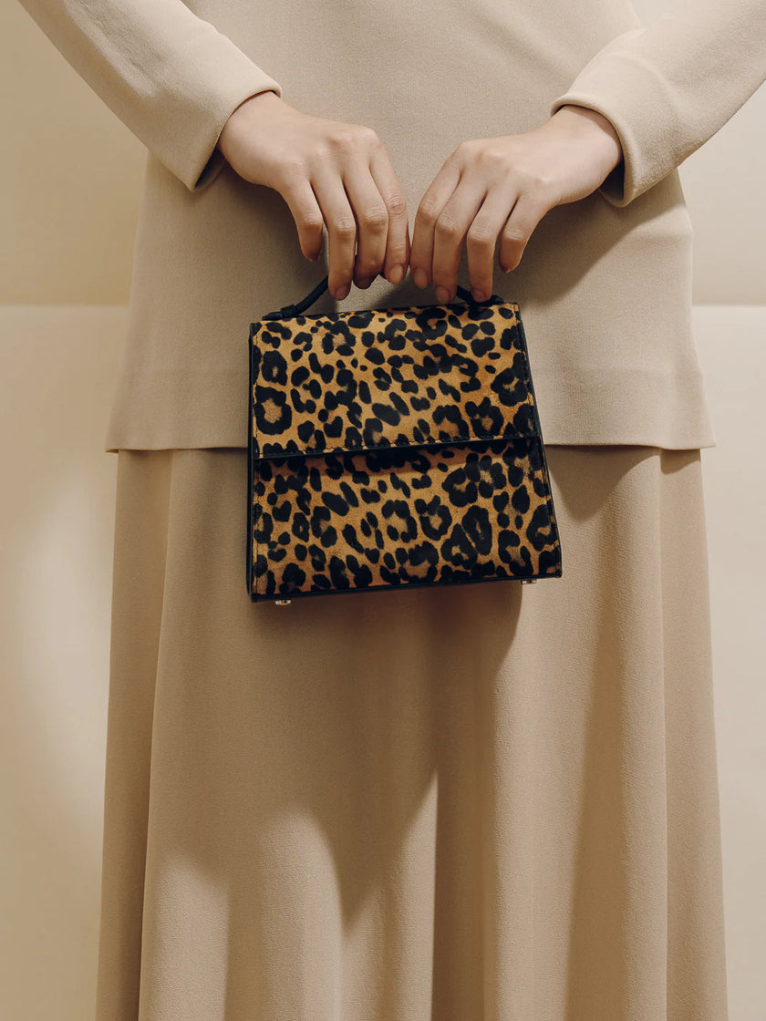 Person holding a leopard print handbag against a neutral background