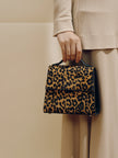 Person holding a leopard print handbag against a neutral background