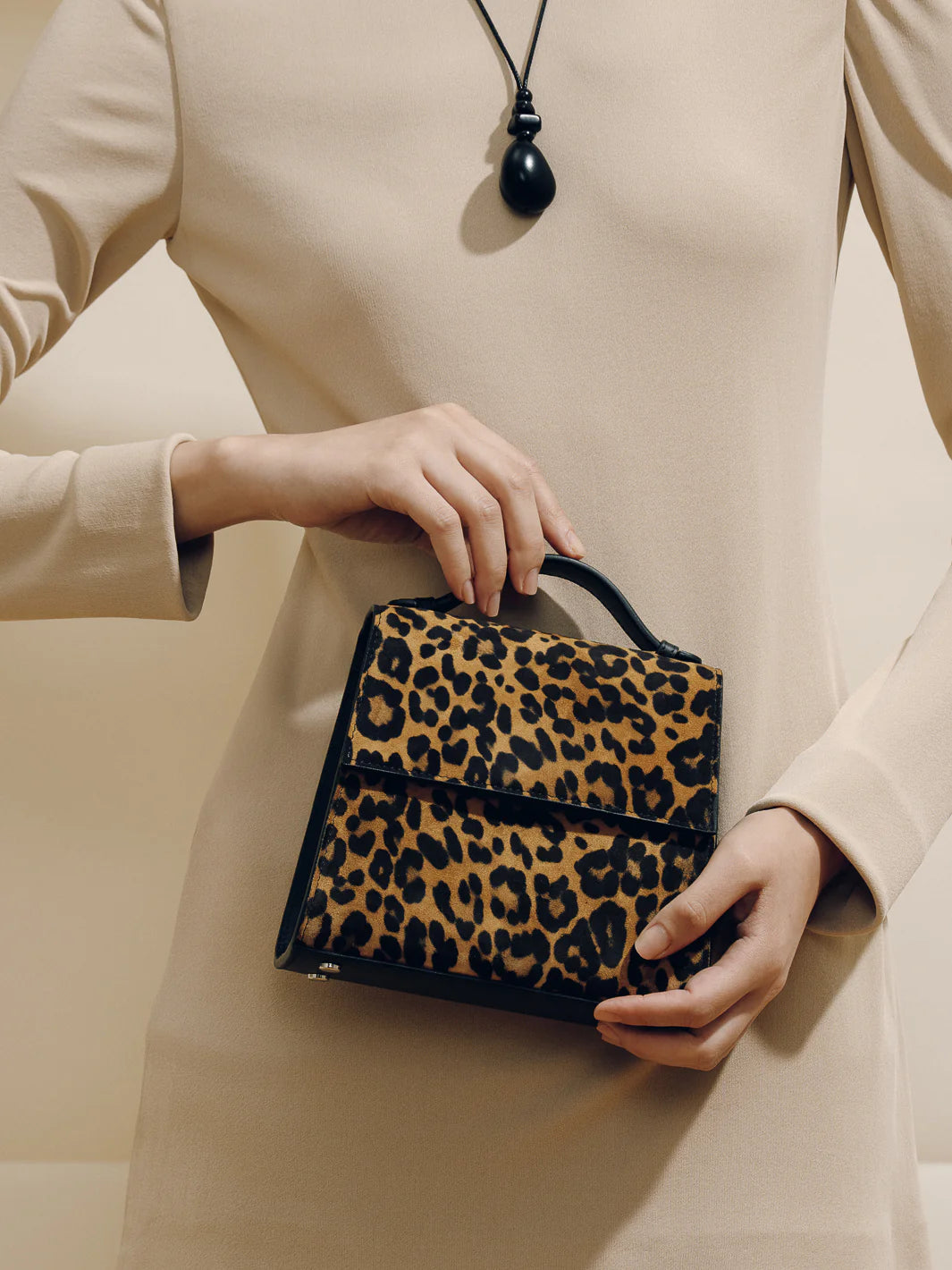 Person holding a leopard print handbag against a neutral background