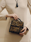 Person holding a leopard print handbag against a neutral background