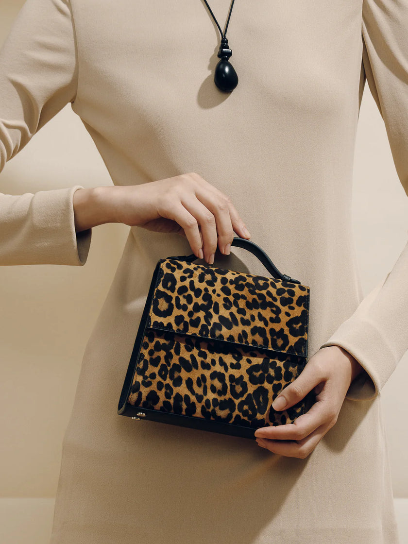 Person holding a leopard print handbag against a neutral background