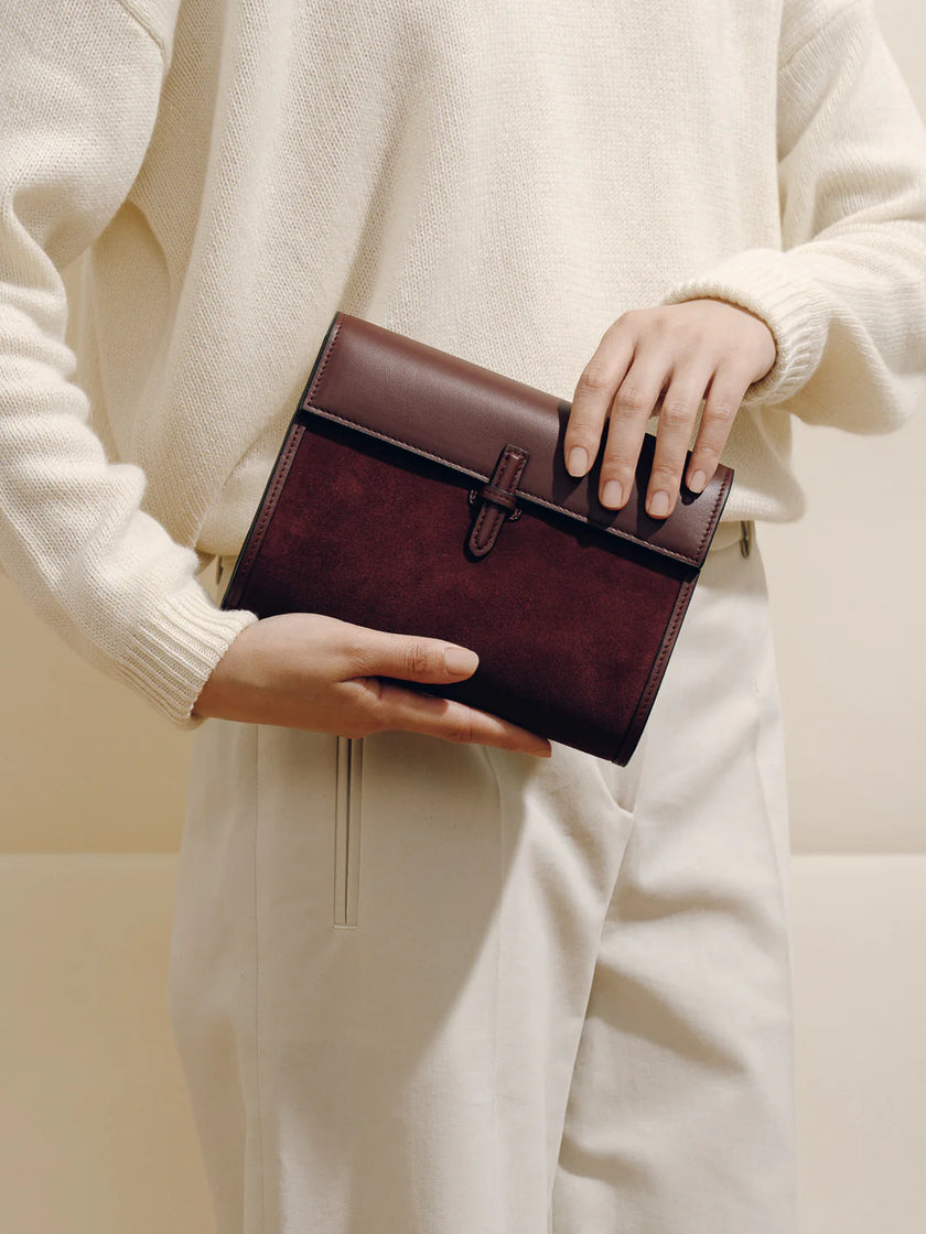 Person holding a brown leather clutch against a neutral background