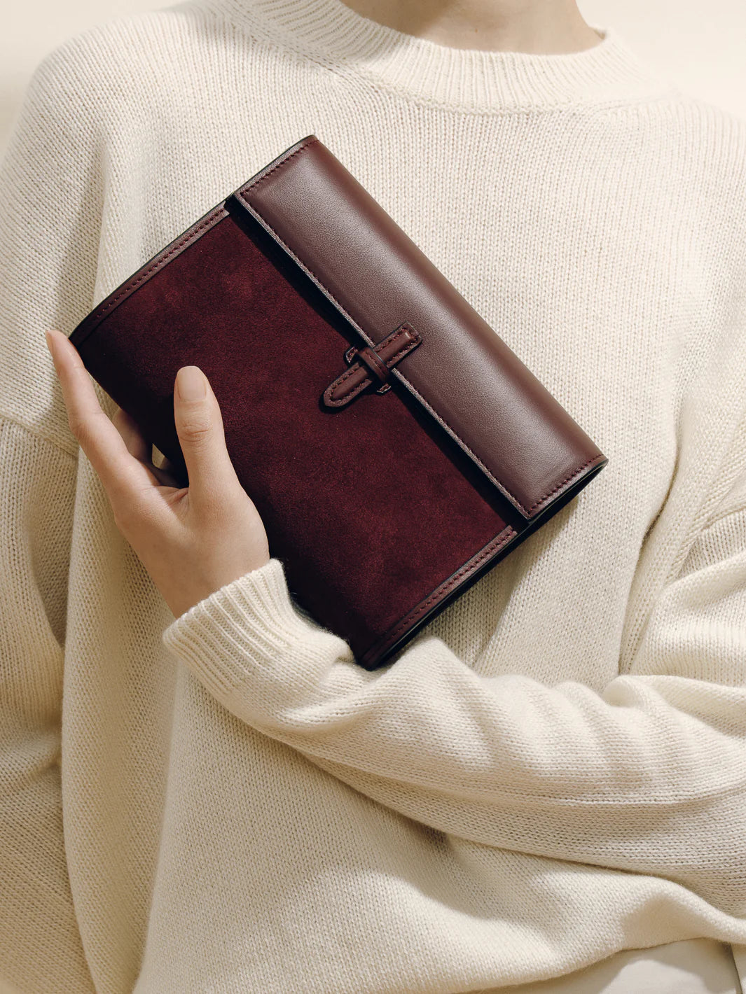 Brown leather wallet held by a person wearing a beige sweater
