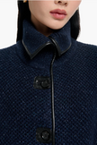 Close-up of a navy blue coat with leather trim and buttons on a white background
